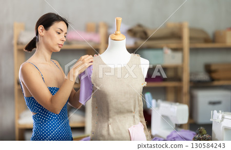 Woman seamstress adjusts clothes on mannequin Woman seamstress adjusts clothes on mannequin 130584243