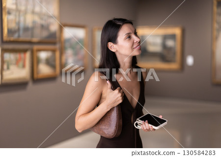 Brunette with phone in hand came to the art gallery 130584283