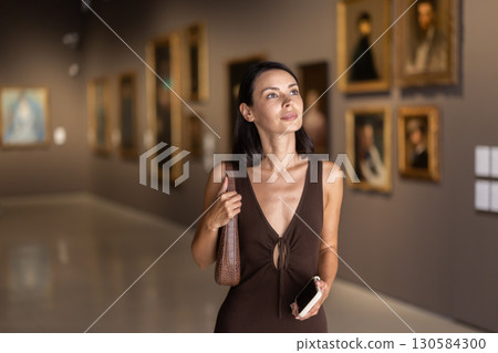 Woman visiting museum and looking at paintings in gold frames 130584300