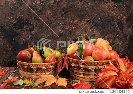 Basket with pears and apples on an old wooden table.Autumn abstract composition with maple leaves, thanksgiving day concepts, background, banner or splash screen, postcard, selective focus .. 130584395