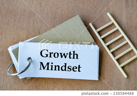 Notepad beside miniature ladder displaying Growth Mindset handwritten neatly in black. Notepad beside miniature ladder displaying Growth Mindset handwritten neatly in black. 130584488
