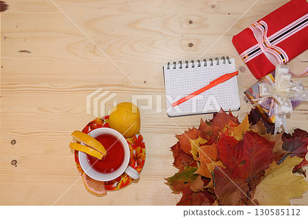 Thanksgiving, autumn background with seasonal maple leaves, a cup of hot tea with lemon and gifts on a wooden background, top view, copy space, flat lay. Happy Thanksgiving concept, selective focus. 130585112