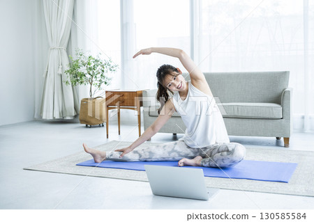 Young woman stretching while looking at a computer at home 130585584
