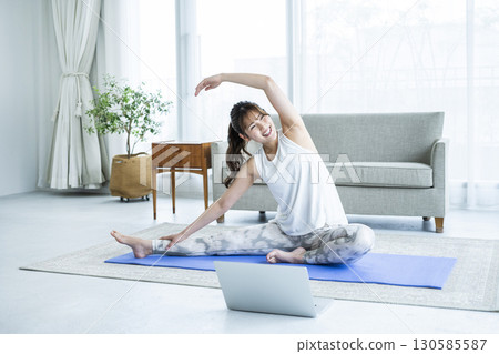 Young woman stretching while looking at a computer at home 130585587