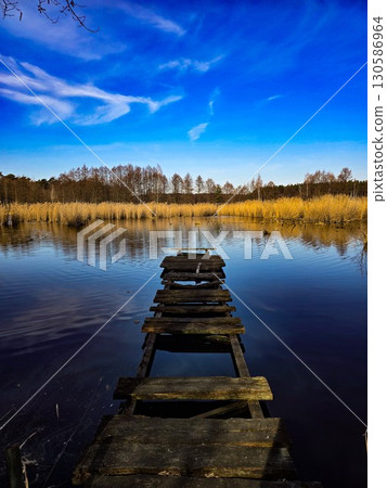 Old Wooden Pier on Calm Lake Under Vibrant Blue Sky Old Wooden Pier on Calm Lake Under Vibrant Blue Sky 130586964