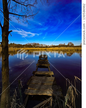 Old Wooden Pier on Calm Lake Under Vibrant Blue Sky Old Wooden Pier on Calm Lake Under Vibrant Blue Sky 130586982