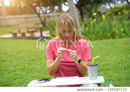 Young woman beading colorful bracelets outdoors in a park Young woman beading colorful bracelets outdoors in a park 130587137