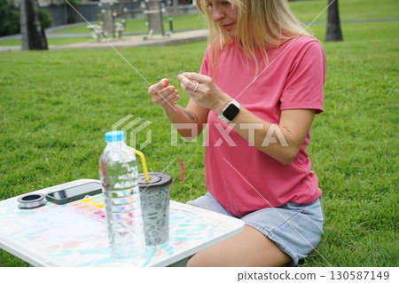 Young woman beading colorful bracelets outdoors in a park 130587149