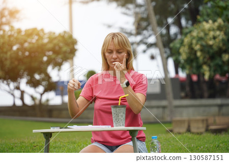 Young woman beading colorful bracelets outdoors in a park Young woman beading colorful bracelets outdoors in a park 130587151