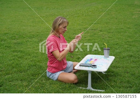 Young woman beading colorful bracelets outdoors in a park Young woman beading colorful bracelets outdoors in a park 130587155