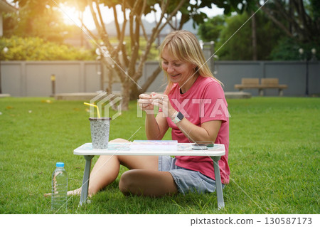 Young woman beading colorful bracelets outdoors in a park Young woman beading colorful bracelets outdoors in a park 130587173