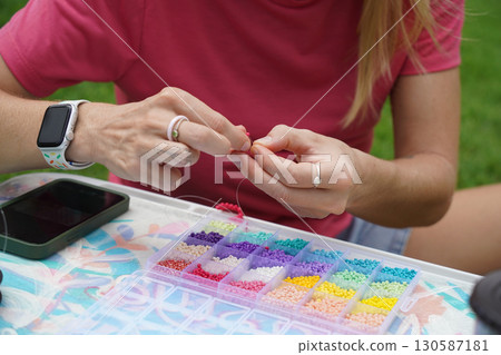 Young woman beading colorful bracelets outdoors in a park Young woman beading colorful bracelets outdoors in a park 130587181