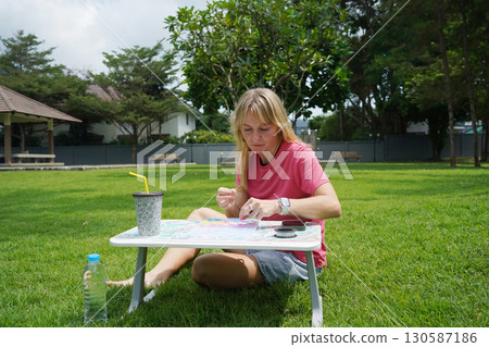 Young woman beading colorful bracelets outdoors in a park 130587186