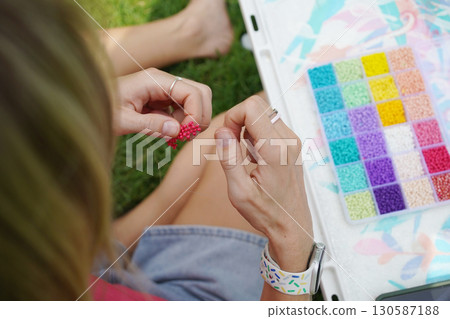 Young woman beading colorful bracelets outdoors in a park 130587188