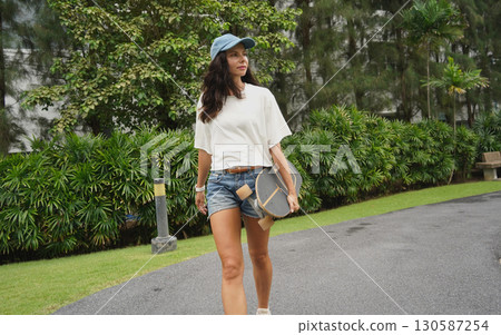 A woman is walking at the city park while carrying a skateboard in her hands 130587254