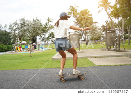 A young woman is skillfully riding a skateboard down a scenic park A young woman is skillfully riding a skateboard down a scenic park 130587257