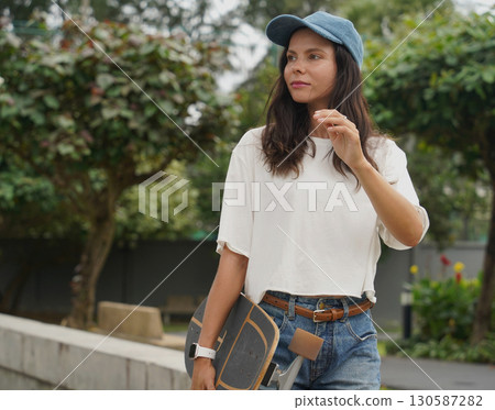 A woman is walking at the city park while carrying a skateboard in her hands 130587282