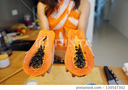 Young woman cuts and peels papaya on the cutting board 130587302