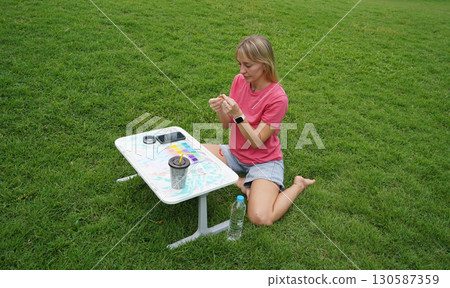 Young woman beading colorful bracelets outdoors in a park Young woman beading colorful bracelets outdoors in a park 130587359