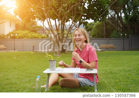 Young woman beading colorful bracelets outdoors in a park Young woman beading colorful bracelets outdoors in a park 130587366