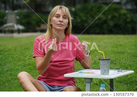 Young woman beading colorful bracelets outdoors in a park 130587370