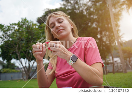 Young woman beading colorful bracelets outdoors in a park 130587380