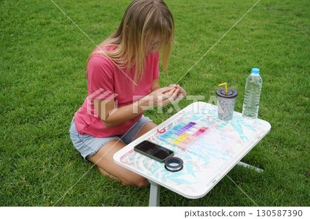 Young woman beading colorful bracelets outdoors in a park 130587390