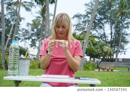 Young woman beading colorful bracelets outdoors in a park 130587393