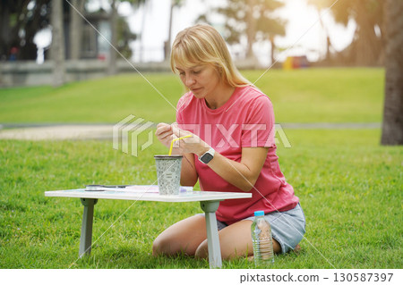 Young woman beading colorful bracelets outdoors in a park Young woman beading colorful bracelets outdoors in a park 130587397