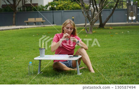Young woman beading colorful bracelets outdoors in a park Young woman beading colorful bracelets outdoors in a park 130587494