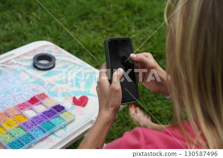 Young woman beading colorful bracelets outdoors in a park Young woman beading colorful bracelets outdoors in a park 130587496