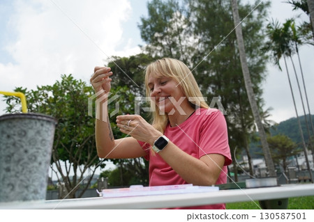 Young woman beading colorful bracelets outdoors in a park 130587501