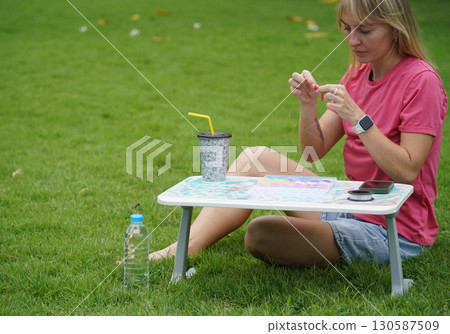Young woman beading colorful bracelets outdoors in a park 130587509