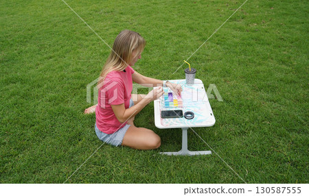 Young woman beading colorful bracelets outdoors in a park Young woman beading colorful bracelets outdoors in a park 130587555