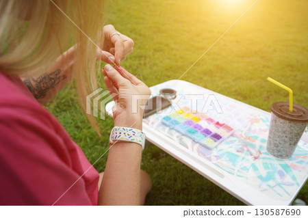 Young woman beading colorful bracelets outdoors in a park Young woman beading colorful bracelets outdoors in a park 130587690