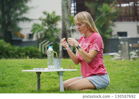 Young woman beading colorful bracelets outdoors in a park Young woman beading colorful bracelets outdoors in a park 130587692