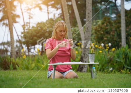 Young woman beading colorful bracelets outdoors in a park Young woman beading colorful bracelets outdoors in a park 130587696