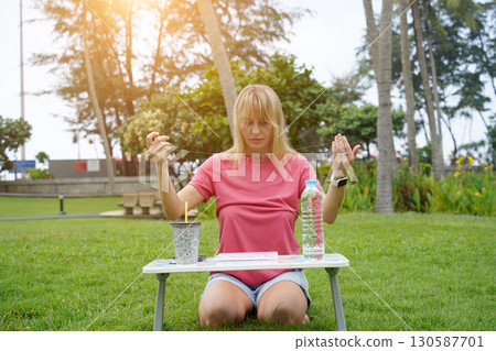 Young woman beading colorful bracelets outdoors in a park Young woman beading colorful bracelets outdoors in a park 130587701