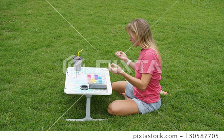 Young woman beading colorful bracelets outdoors in a park Young woman beading colorful bracelets outdoors in a park 130587705
