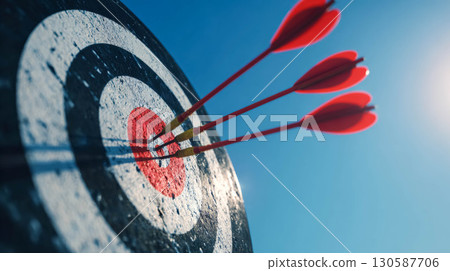 Red arrows striking a bullseye on a target against a clear blue sky with sunlight shining 130587706