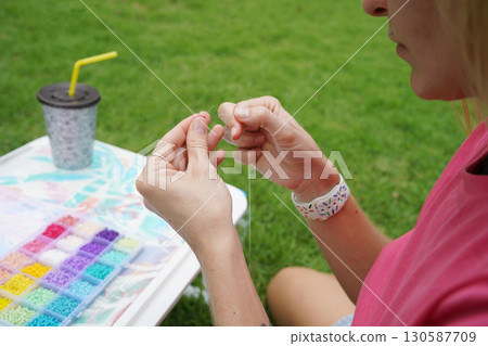 Young woman beading colorful bracelets outdoors in a park Young woman beading colorful bracelets outdoors in a park 130587709