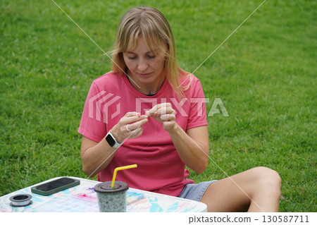Young woman beading colorful bracelets outdoors in a park Young woman beading colorful bracelets outdoors in a park 130587711