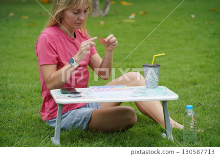 Young woman beading colorful bracelets outdoors in a park Young woman beading colorful bracelets outdoors in a park 130587713