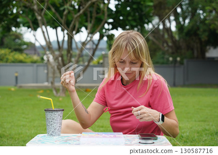 Young woman beading colorful bracelets outdoors in a park Young woman beading colorful bracelets outdoors in a park 130587716