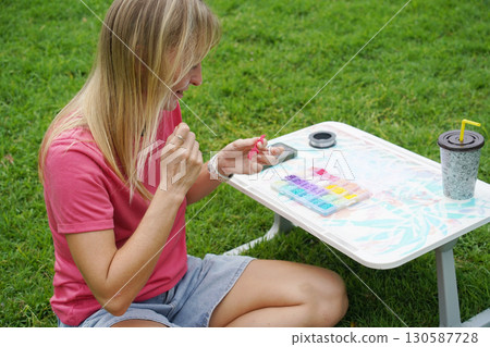 Young woman beading colorful bracelets outdoors in a park Young woman beading colorful bracelets outdoors in a park 130587728