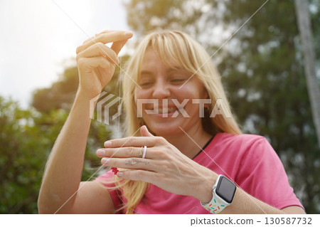 Young woman beading colorful bracelets outdoors in a park Young woman beading colorful bracelets outdoors in a park 130587732