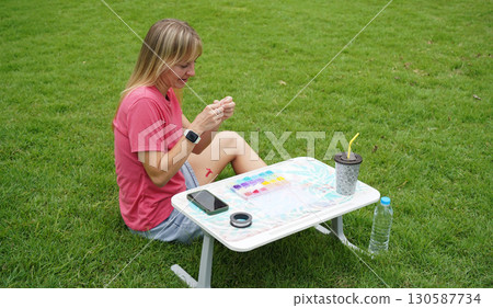 Young woman beading colorful bracelets outdoors in a park 130587734