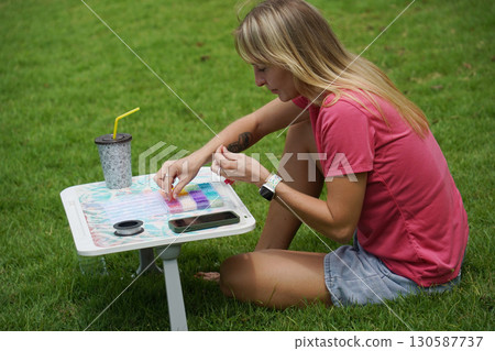 Young woman beading colorful bracelets outdoors in a park Young woman beading colorful bracelets outdoors in a park 130587737