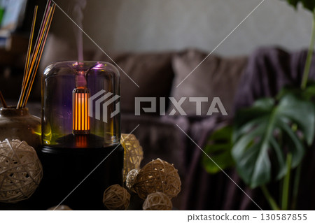 Close up of home perfume scent air humidifier with light. Aromatherapy holistic health practices concept. Stress relief activities preparing for meditation. Simple pleasures healing Close up of home perfume scent air humidifier with light. Aromatherapy holistic health practices concept. Stress relief activities preparing for meditation. Simple pleasures healing 130587855