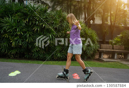 A woman is rollerblading gracefully on a road located in a park 130587884